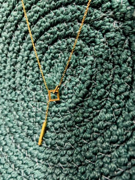 Geometric anti-tarnish gold pendant necklace on textured green background