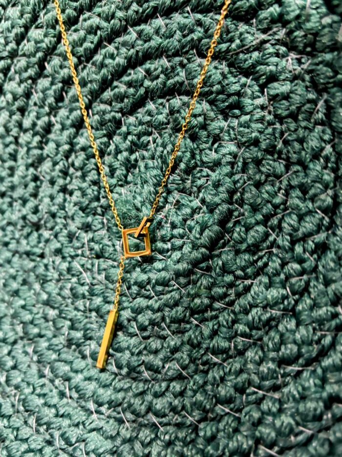Geometric anti-tarnish gold pendant necklace on textured green background