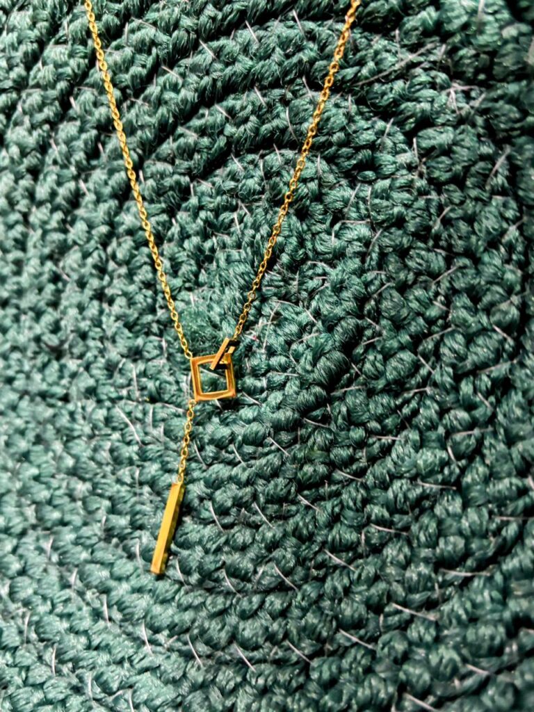 Geometric anti-tarnish gold pendant necklace on textured green background